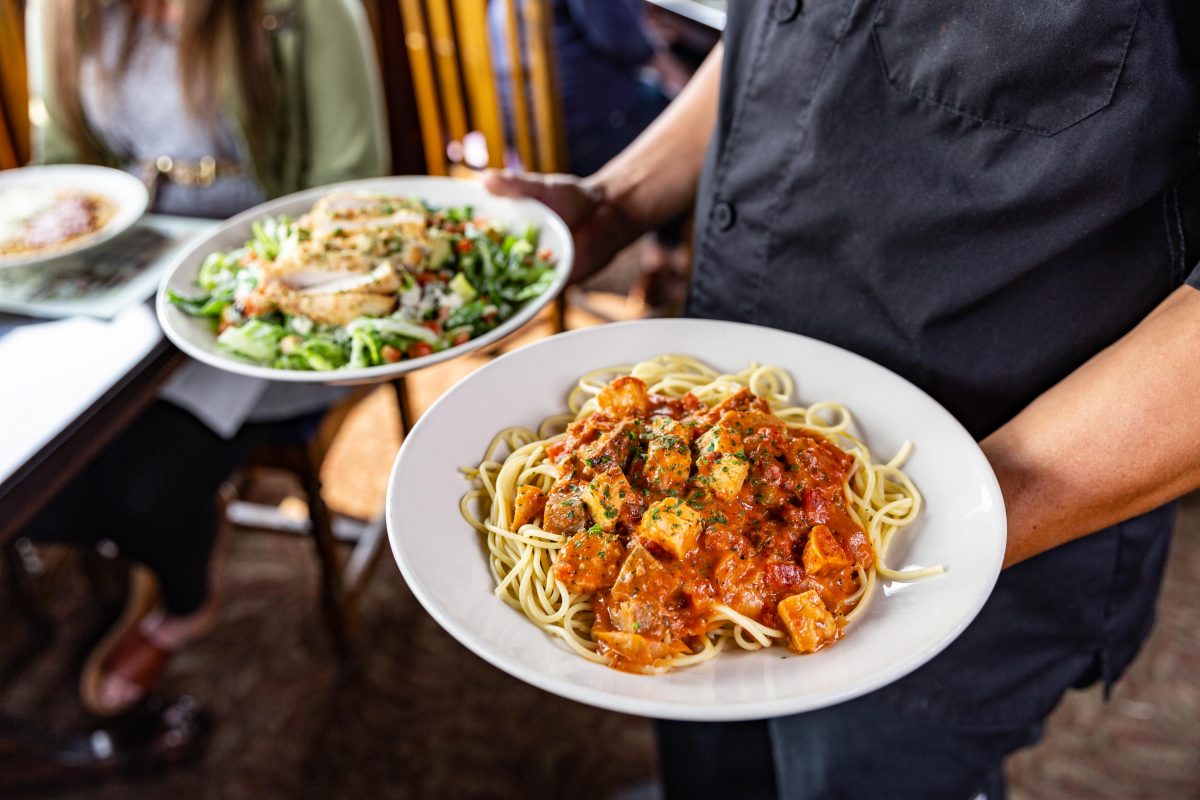 server carrying plate of pasta and plate of salad at The Old Spaghetti Factory