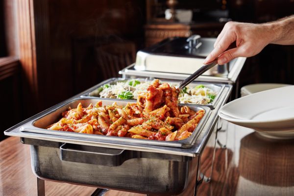 plate being filled at catering trays of pasta